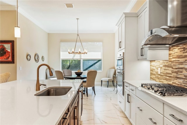 kitchen with stainless steel appliances, sink, wall chimney range hood, an inviting chandelier, and white cabinetry