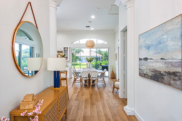 hall featuring light hardwood / wood-style floors, a healthy amount of sunlight, ornate columns, and crown molding