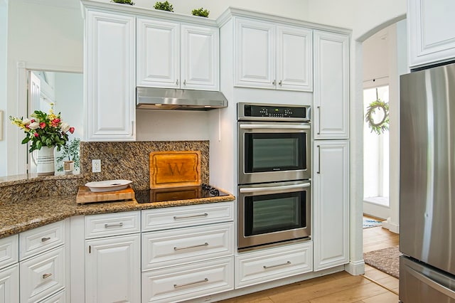 kitchen featuring tasteful backsplash, dark stone counters, appliances with stainless steel finishes, white cabinets, and light hardwood / wood-style flooring