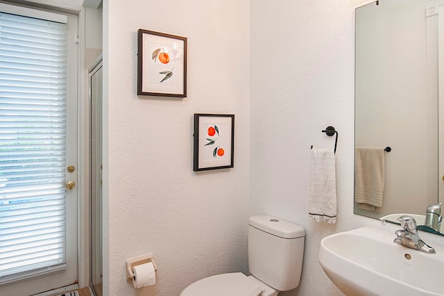 bathroom with toilet, a wealth of natural light, sink, and a shower with door