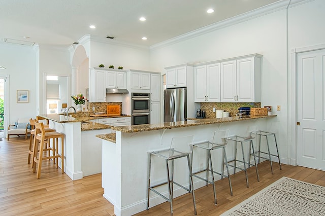 kitchen featuring white cabinets, kitchen peninsula, a breakfast bar, light wood-type flooring, and appliances with stainless steel finishes