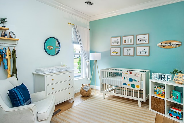 bedroom with crown molding, light hardwood / wood-style floors, and a crib