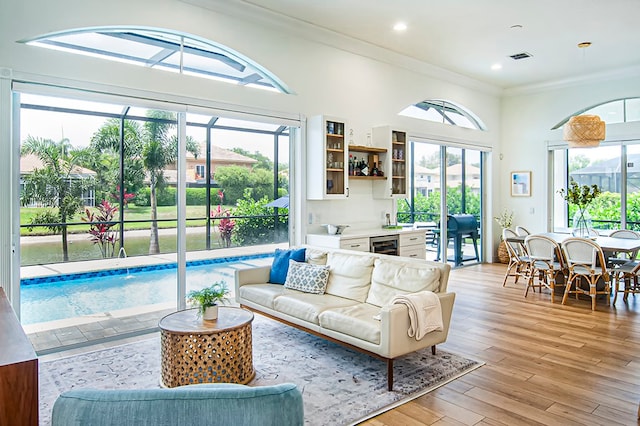 living room featuring a wealth of natural light, crown molding, wine cooler, and light hardwood / wood-style floors