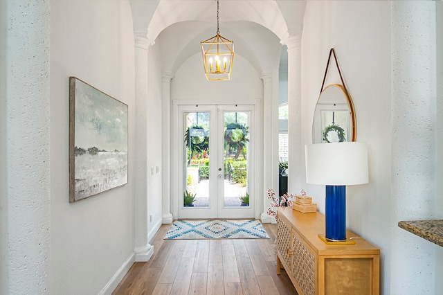 foyer entrance with ornate columns, french doors, a notable chandelier, and hardwood / wood-style flooring