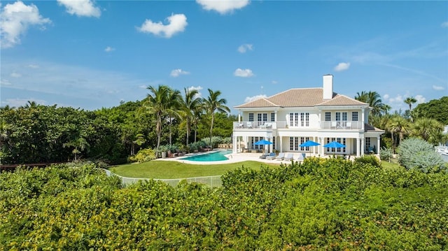 back of property with a balcony, a patio, and a lawn