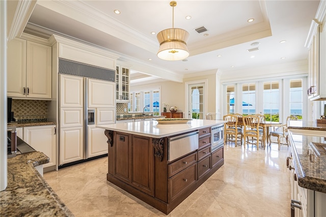 kitchen featuring built in appliances, a center island, decorative light fixtures, a tray ceiling, and light stone countertops