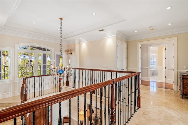 hallway featuring a raised ceiling, ornamental molding, and an inviting chandelier