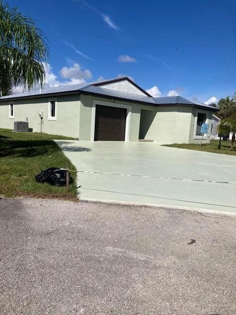 view of front of home with a front lawn, central AC unit, and a garage