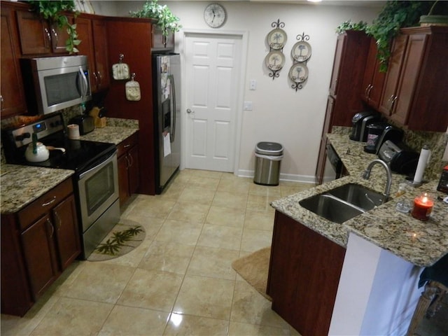 kitchen with light stone countertops, sink, stainless steel appliances, kitchen peninsula, and light tile patterned flooring