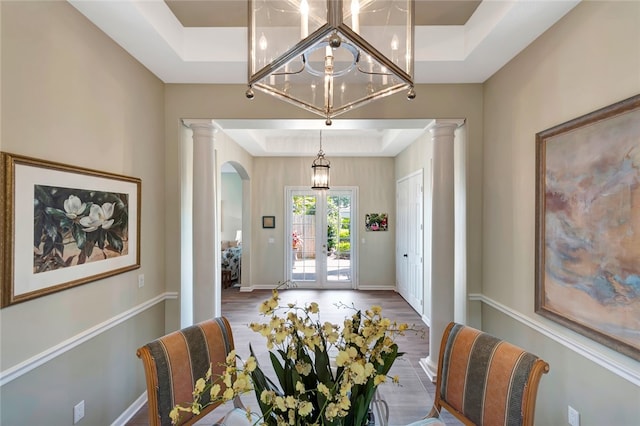 dining space with hardwood / wood-style floors, decorative columns, french doors, and a raised ceiling