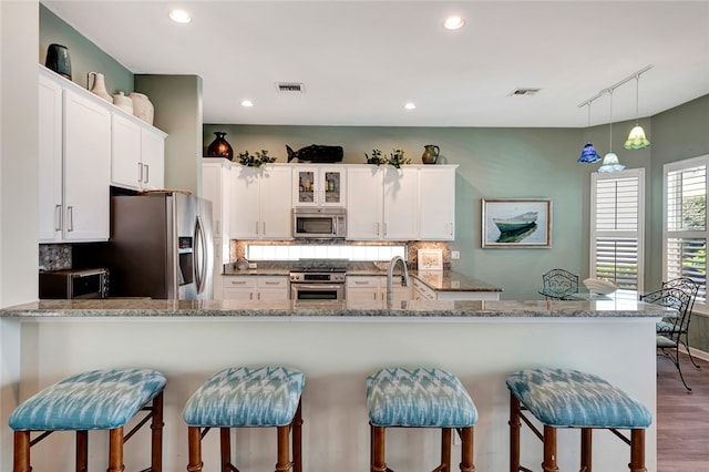 kitchen with white cabinetry, kitchen peninsula, stainless steel appliances, and wood-type flooring