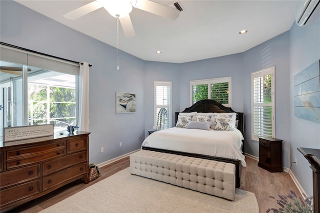 bedroom featuring a wall mounted AC, hardwood / wood-style flooring, multiple windows, and ceiling fan