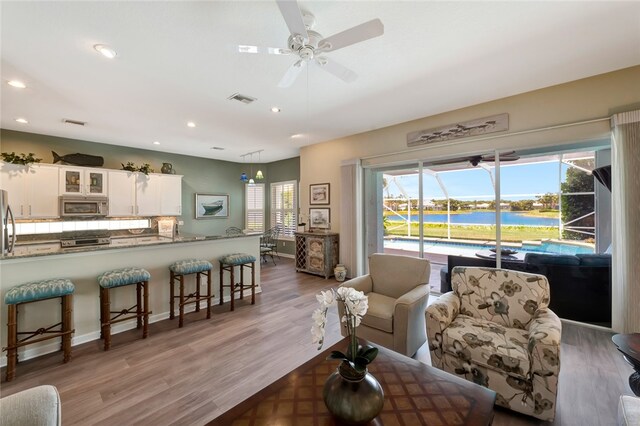 living room with a water view, hardwood / wood-style flooring, and ceiling fan