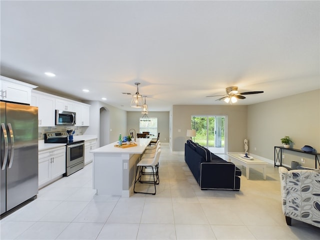 kitchen with a center island with sink, appliances with stainless steel finishes, a kitchen bar, hanging light fixtures, and white cabinets