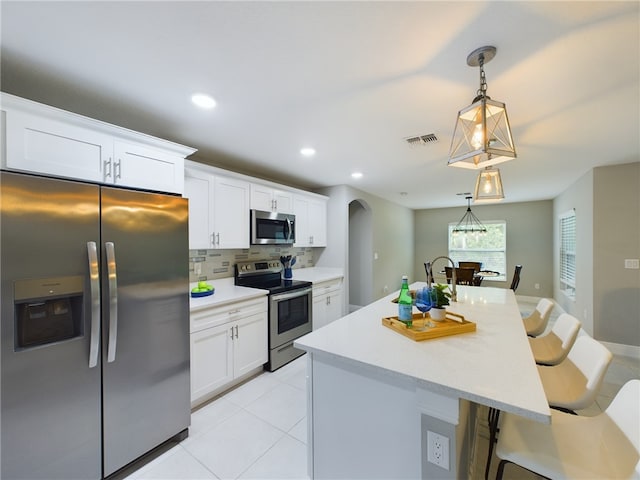 kitchen with white cabinetry, appliances with stainless steel finishes, decorative light fixtures, backsplash, and a breakfast bar area