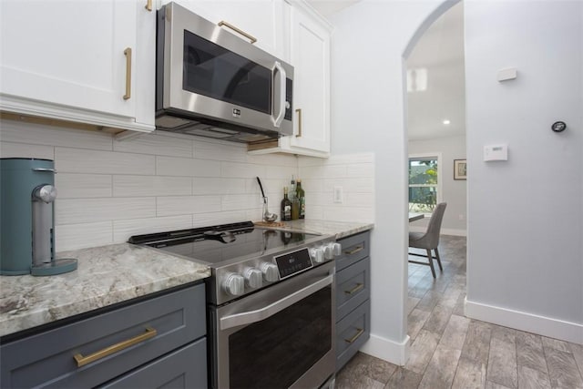 kitchen featuring white cabinetry, appliances with stainless steel finishes, light stone counters, and decorative backsplash