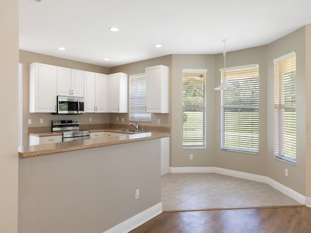 kitchen with white cabinetry, sink, appliances with stainless steel finishes, light hardwood / wood-style flooring, and pendant lighting