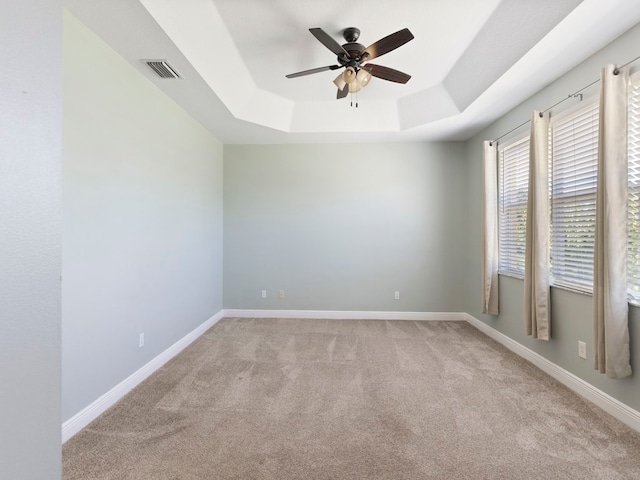 spare room featuring ceiling fan, light colored carpet, and a tray ceiling