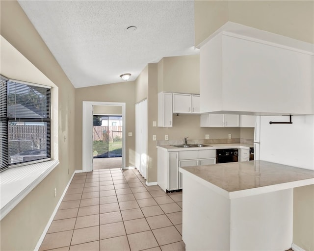 kitchen featuring sink, kitchen peninsula, vaulted ceiling, light tile patterned floors, and white cabinetry