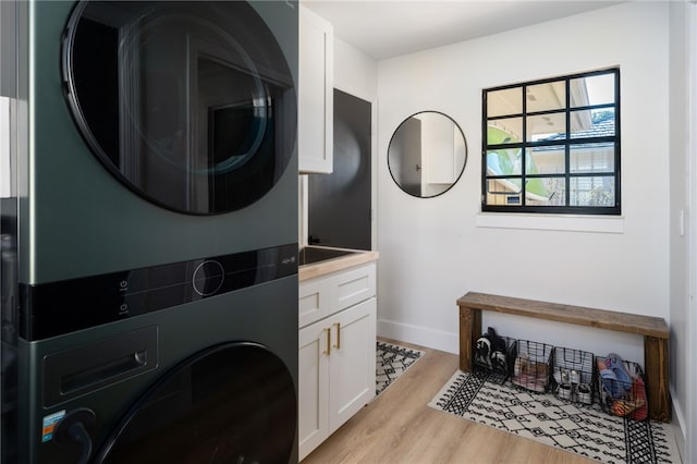 laundry area with cabinets, stacked washer and dryer, and light hardwood / wood-style flooring