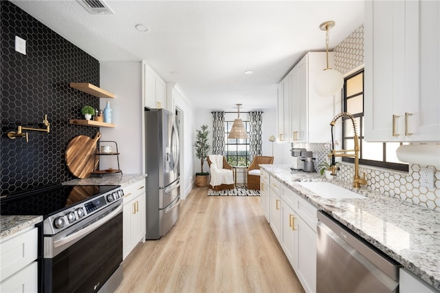 kitchen with sink, white cabinetry, light stone counters, appliances with stainless steel finishes, and pendant lighting