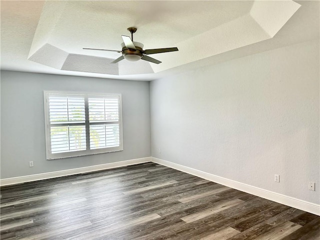 unfurnished room featuring ceiling fan, baseboards, a raised ceiling, and dark wood-type flooring