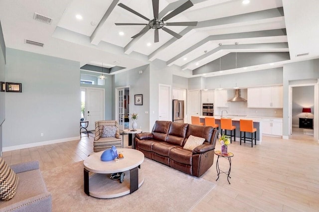 living room with beam ceiling, ceiling fan, sink, light hardwood / wood-style flooring, and high vaulted ceiling