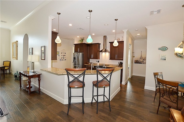 kitchen featuring kitchen peninsula, ornamental molding, stainless steel refrigerator with ice dispenser, wall chimney exhaust hood, and dark wood-type flooring