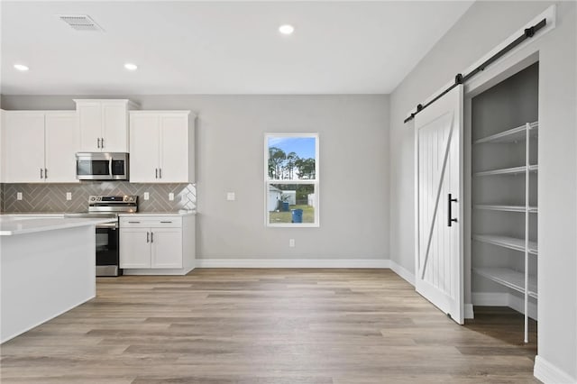 kitchen with white cabinetry, stainless steel appliances, a barn door, and light hardwood / wood-style floors