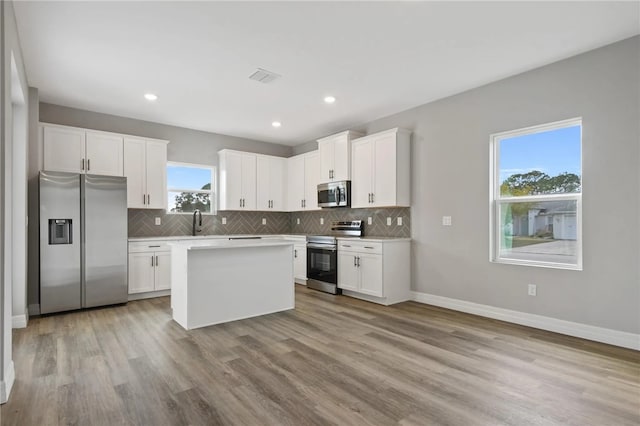 kitchen with sink, white cabinets, a center island, stainless steel appliances, and light hardwood / wood-style flooring