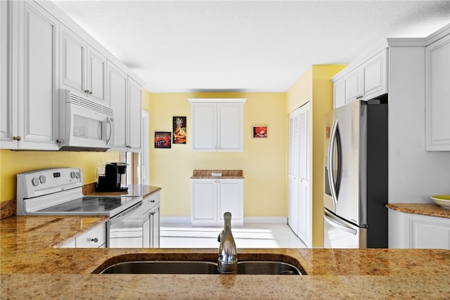 kitchen with white cabinetry, sink, white appliances, and light stone countertops