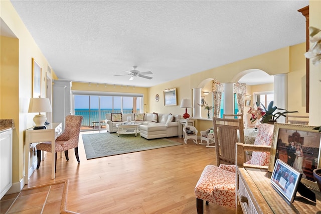 living room featuring light wood-type flooring, a water view, a textured ceiling, and a healthy amount of sunlight