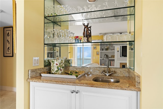 bar with sink, light stone counters, and white cabinets