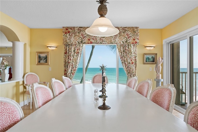 dining space featuring a wealth of natural light, wood-type flooring, a water view, and decorative columns