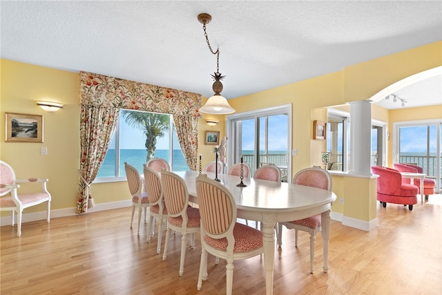 dining room with light hardwood / wood-style flooring, a textured ceiling, a water view, and decorative columns