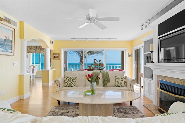 living room with a premium fireplace, decorative columns, rail lighting, ceiling fan, and light wood-type flooring