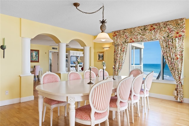 dining space with a water view, a textured ceiling, ornate columns, and light hardwood / wood-style flooring