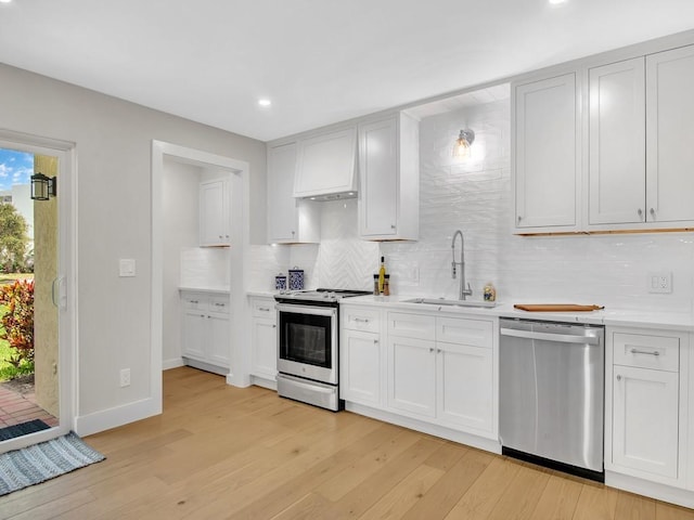 kitchen with sink, white cabinetry, light hardwood / wood-style flooring, decorative backsplash, and appliances with stainless steel finishes