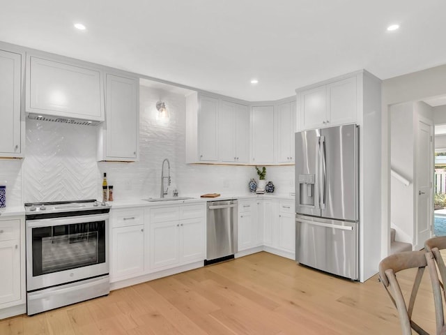 kitchen with light hardwood / wood-style floors, backsplash, white cabinets, appliances with stainless steel finishes, and sink