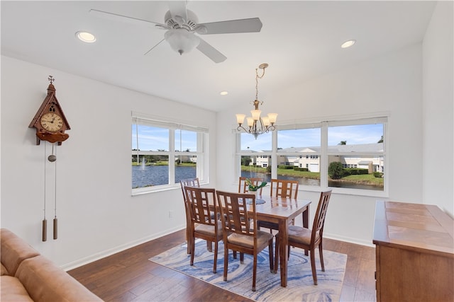 dining area with ceiling fan with notable chandelier, dark hardwood / wood-style floors, and a water view