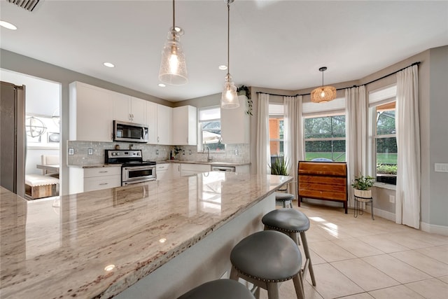 kitchen with appliances with stainless steel finishes, light stone counters, a healthy amount of sunlight, and white cabinets