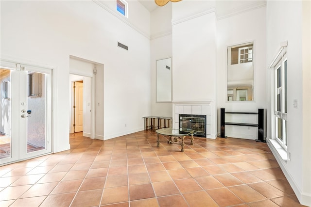 living room featuring a towering ceiling, a fireplace, light tile patterned floors, and crown molding