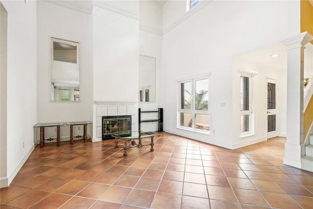 living room featuring tile patterned flooring, ornamental molding, a fireplace, a towering ceiling, and decorative columns