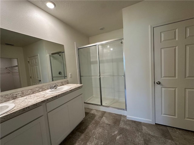 bathroom featuring a walk in closet, a stall shower, a sink, double vanity, and baseboards