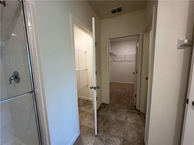 full bathroom featuring visible vents, a walk in closet, a stall shower, stone finish flooring, and baseboards