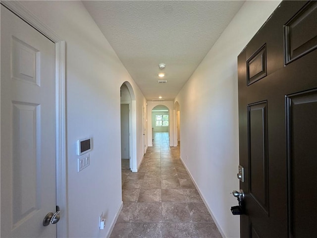 corridor featuring baseboards, arched walkways, and a textured ceiling