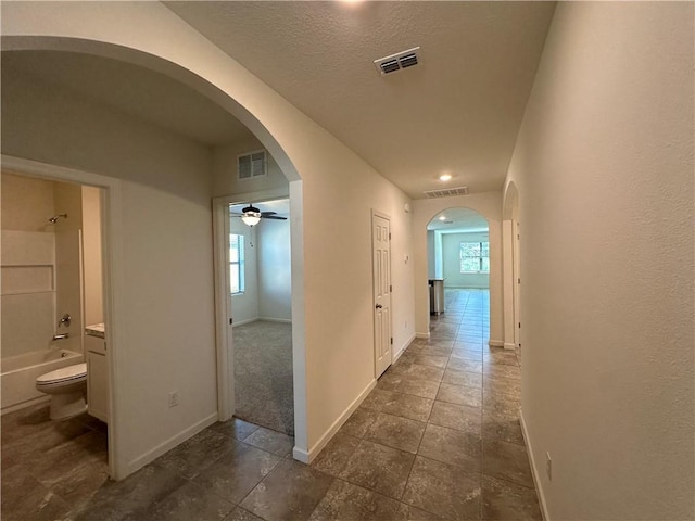 hallway with visible vents, arched walkways, and baseboards