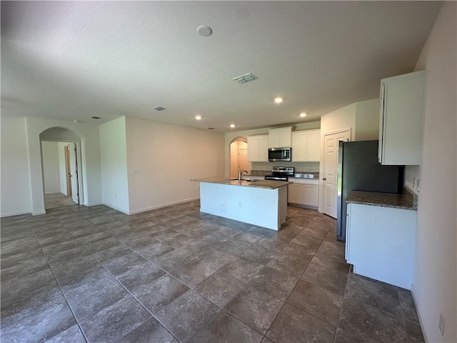 kitchen with visible vents, a center island with sink, a sink, stainless steel appliances, and arched walkways