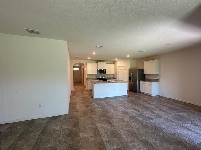 kitchen featuring visible vents, an island with sink, arched walkways, white cabinets, and stainless steel appliances