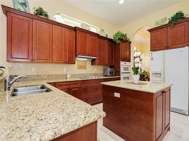 kitchen with tasteful backsplash, a kitchen island, light stone countertops, sink, and white appliances